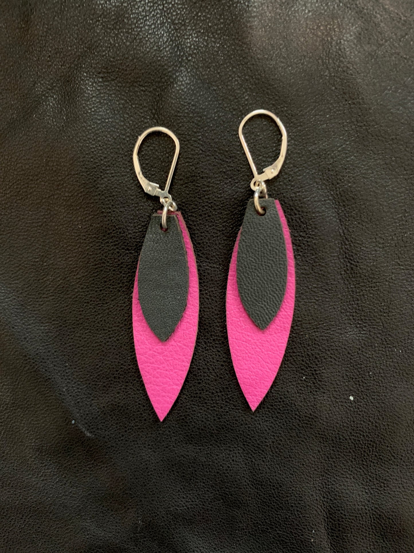 Feather shaped earrings with a layer of pink leather behind a smaller dark grey leather piece hanging from sterling silver lever back ear wires