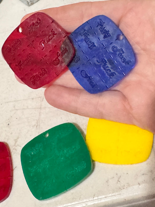 4 pillow shaped plastic keychain pieces that each have the word f*ck engraved on them 6 times separated by perforation marks 